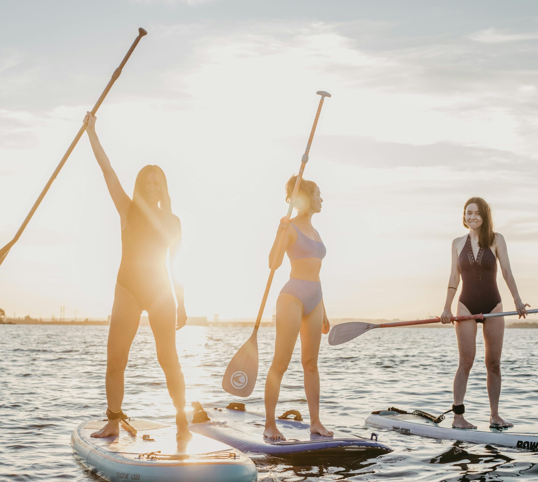 Three women enjoying paddleboarding as the sun sets over the ocean.