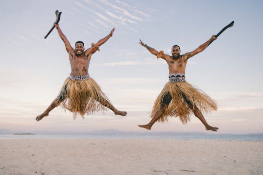Joyful Fijian men in traditional skirts leaping on a beach with the ocean in the background.